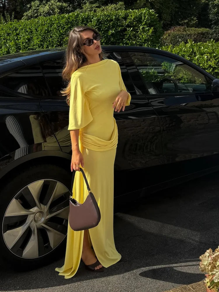 Woman in a yellow dress standing next to a black car outdoors.