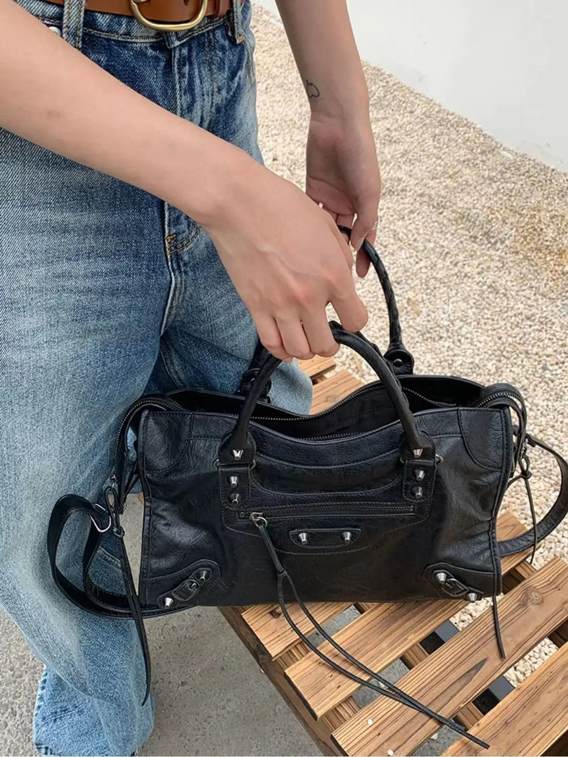 Person holding a black handbag on a wooden surface