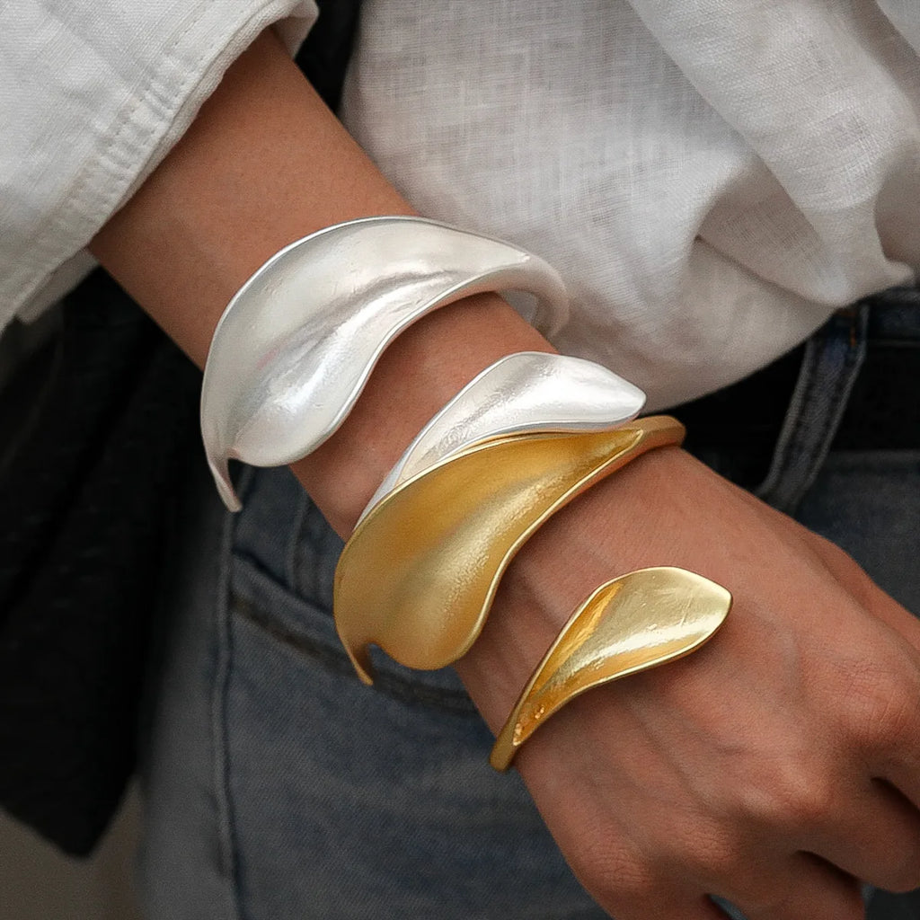 Gold and silver cuff bracelets on a wrist with a blurred background