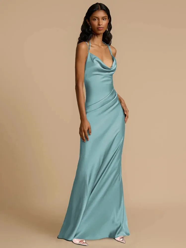 A woman wearing a blue maxi dress with lace back detail, standing against a neutral background.