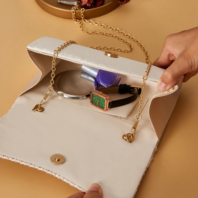 Beige clutch bag with gold chain handle, containing makeup items on a beige background