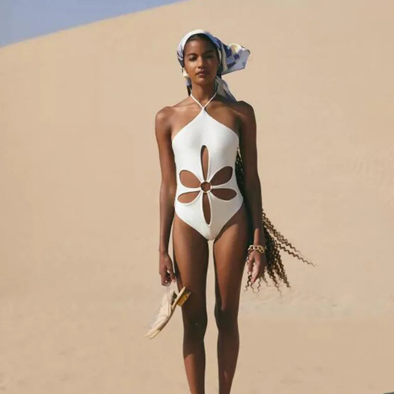Woman in a white swimsuit with floral cutouts standing on sand dunes.