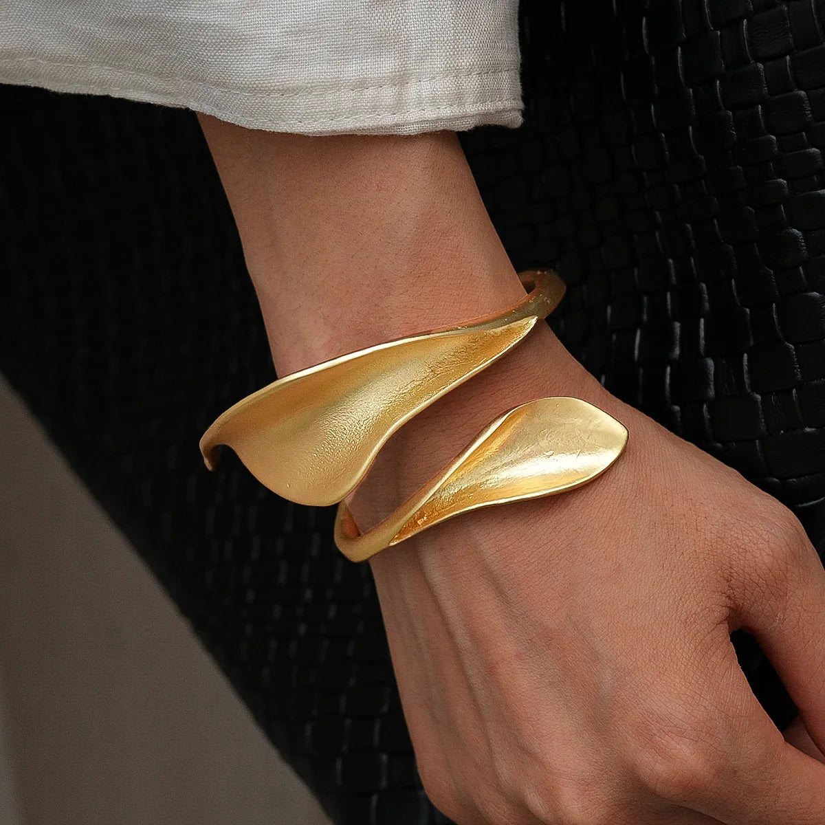 Gold leaf-shaped bracelet on a wrist against a dark woven background