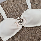 Close-up of a white bikini top with thin straps on a woven surface