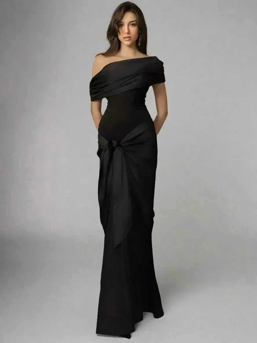 A model wearing a black, floor-length, one-shoulder maxi dress with a V-neck neckline and sleeveless design.