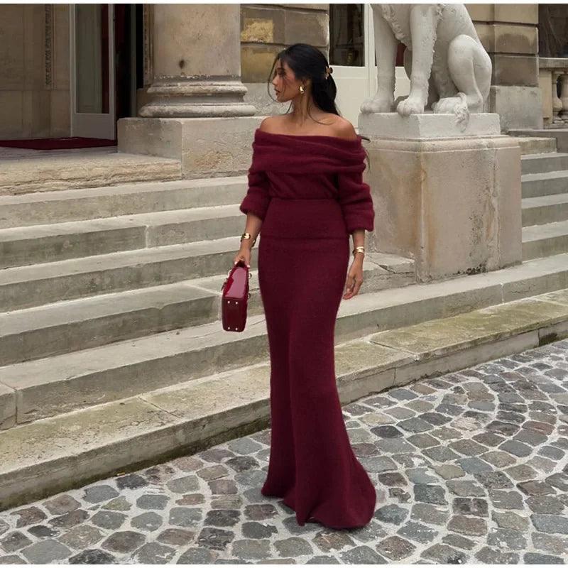 A person wearing a burgundy maxi dress with a Slash neck, long sleeves, and a fitted silhouette, standing outdoors.