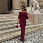 A person wearing a burgundy maxi dress with a Slash neck, long sleeves, and a fitted silhouette, standing outdoors.