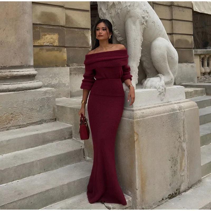 A person wearing a burgundy maxi dress with a Slash neck, long sleeves, and a fitted silhouette, standing outdoors.