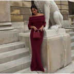A person wearing a burgundy maxi dress with a Slash neck, long sleeves, and a fitted silhouette, standing outdoors.