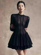 Woman wearing a black dress with a textured pattern on a neutral background.