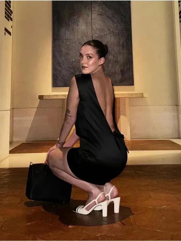 Woman in a black dress posing indoors with a painting in the background.