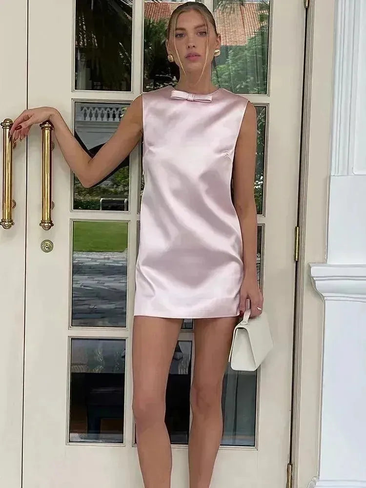Woman in a light pink satin dress standing by a door.