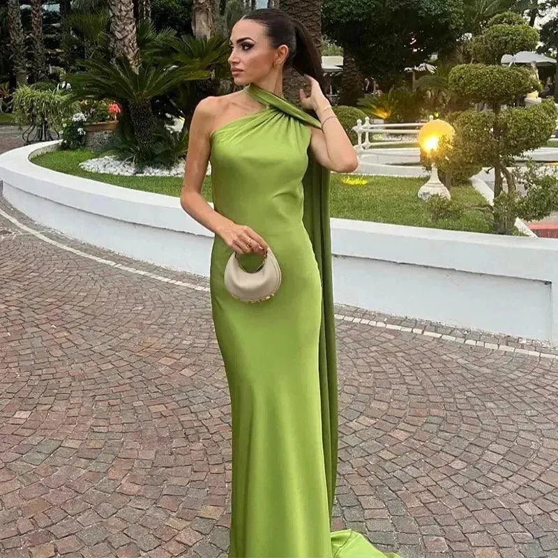 Woman in a green evening gown standing outdoors on a paved path with garden decorations.