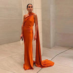 Woman in an orange evening gown standing in a neutral room.