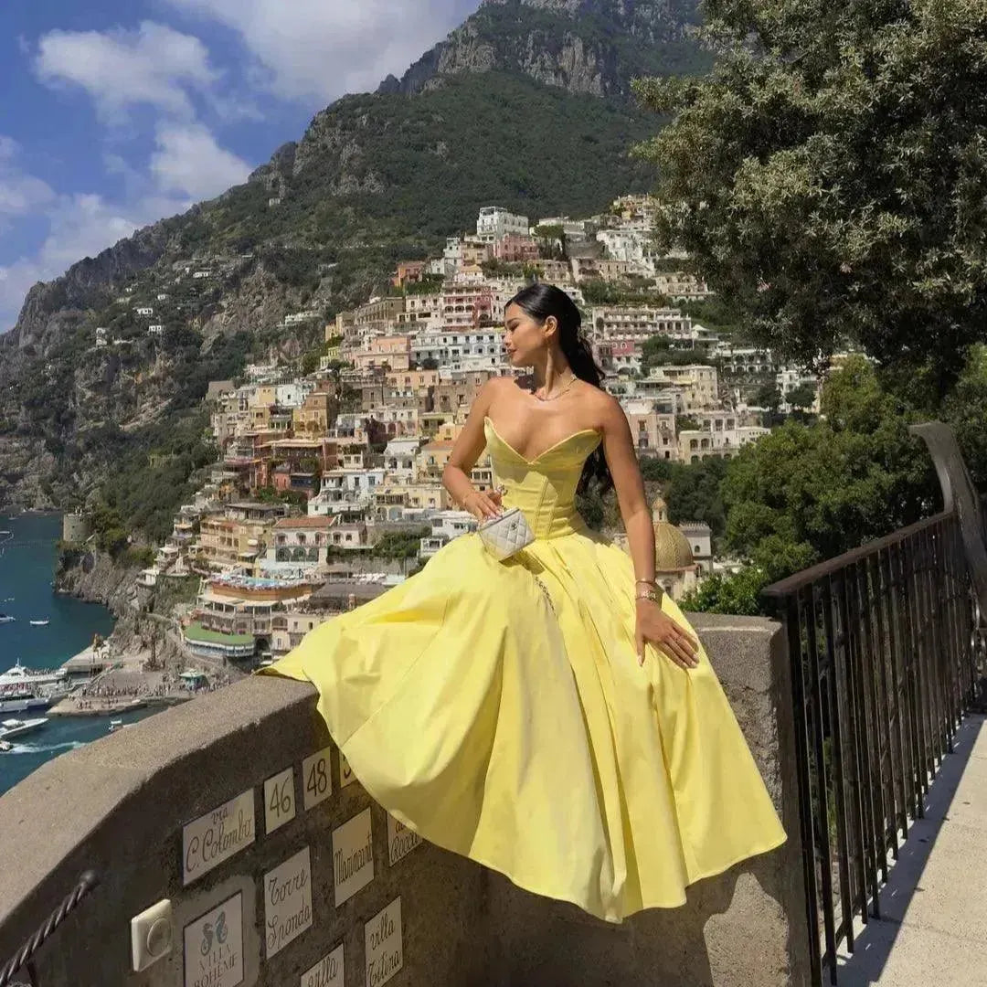 Woman in a yellow dress sitting on a railing with a scenic mountain town view.