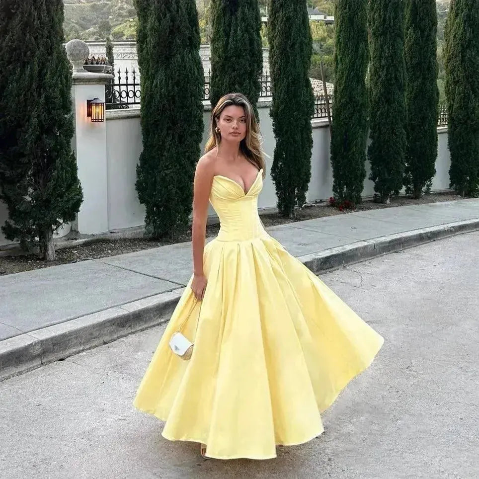 Woman in a yellow dress standing on a path with greenery in the background